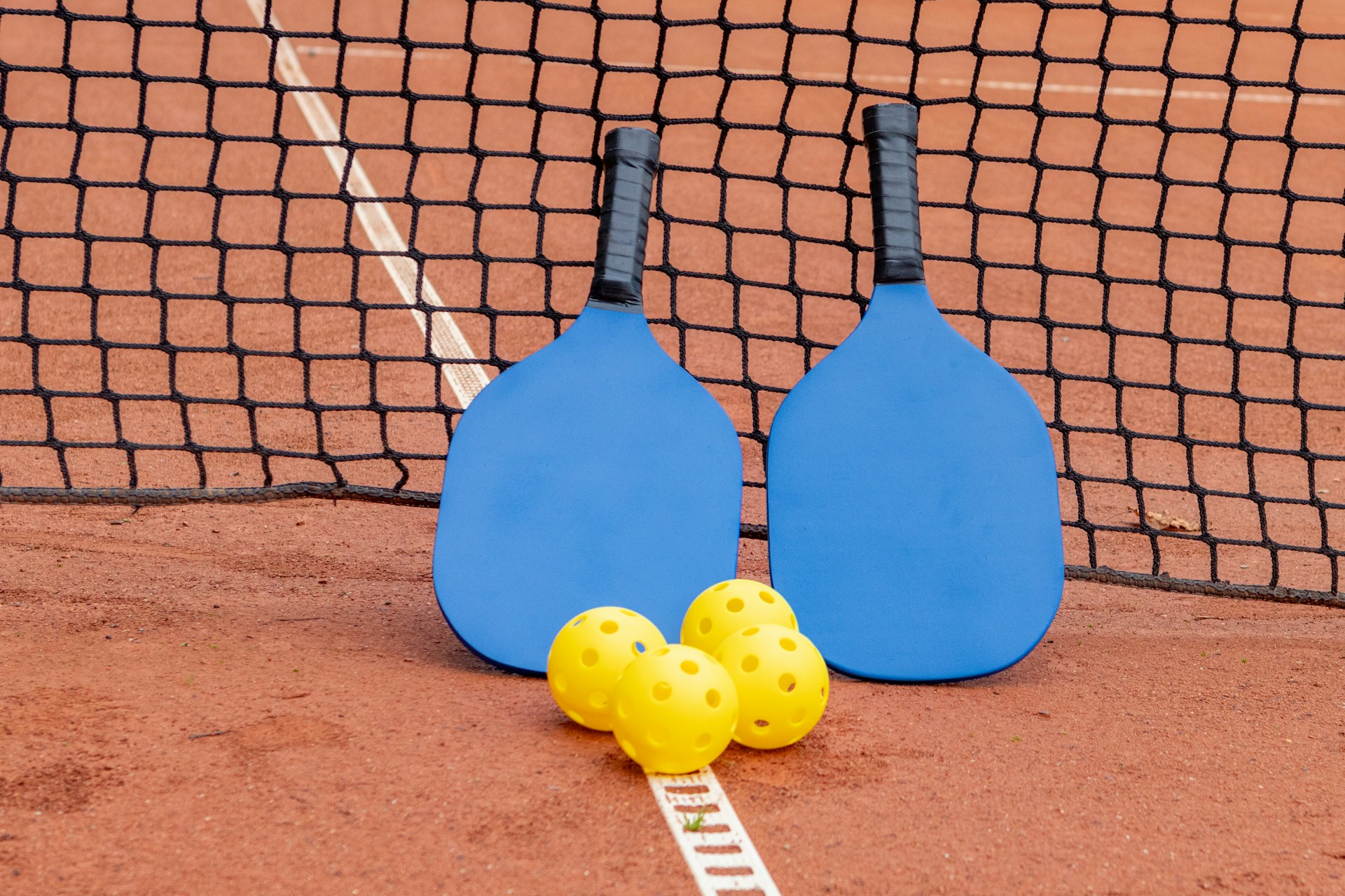 two paddles and three balls on a tennis court